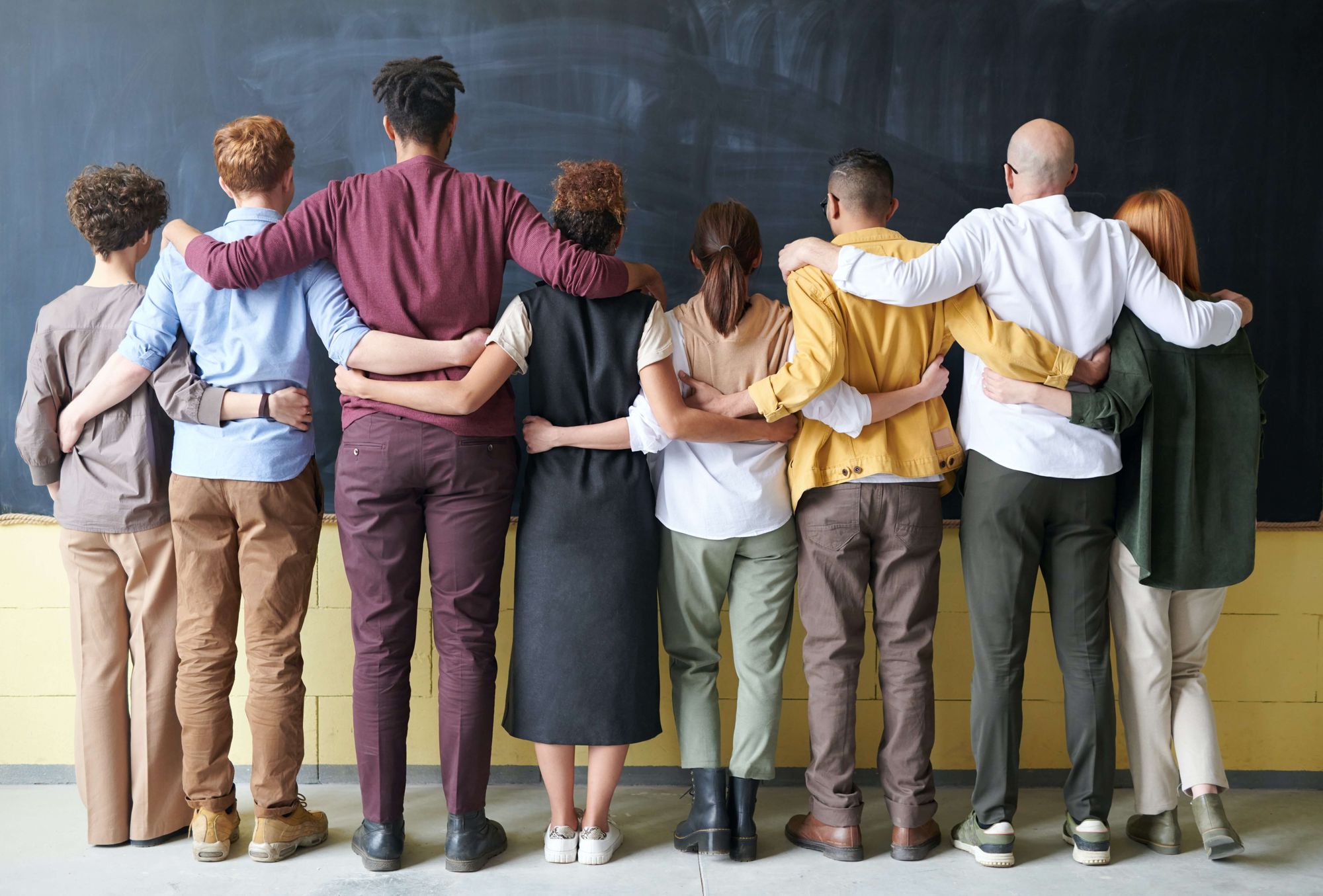 Diverse group of people with their backs to the camera, arms over each other's shoulders